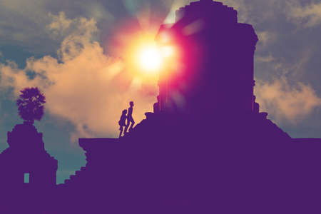 silhouette of two person with sunlight step on stairs to the top of a sacred ancient temple for make...