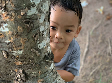 A 1-year adorable Asian kid boy wearing hat portrait standing and holding a white plumeria flower alone in the garden as a headshot closeup, soft backgroundの写真素材