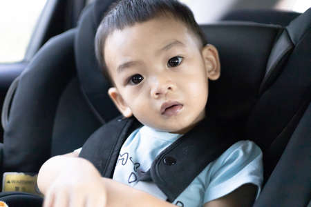 1 Year Old Adorable, an Asian Toddler Boy, Sitting in a Car Seat on a Car While Traveling Looking at the camera. Family Trips and Baby Care and Safety Concept. Front View Closeup Blurry Background.の写真素材
