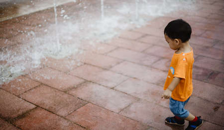 An adorable toddler Asian boy (1-year-old) standing and enjoy to see outdoor public fountains a water splashing for the first time. Thailand plays and fun space for kids. Vacation and holiday concept.の写真素材