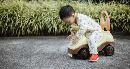 An adorable toddler Asian boy (1-year-old) siting and enjoy to play Ride-on toys outdoor in the garden with grass background. Safety play space for kids. Happy son's activity and lifestyle concept.の写真素材