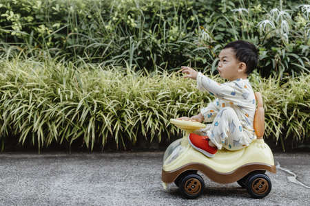 An adorable toddler Asian boy (1-year-old) siting and enjoy to play Ride-on toys outdoor in the...