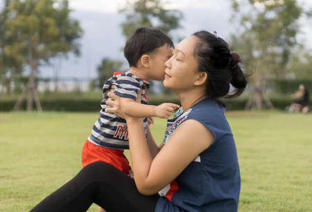 An Asian mother and toddler son (1-year-old) are playing, laugh, and relax together in the garden on a cloudy day. Full-length outdoor portrait happy and fun in public space ideas for family time.の写真素材