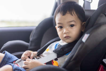 Adorable Asian kid boy (Toddler age 1-year-old) Protection Sitting in the Car Seat with Safety Belt Locked. Family Journey and Baby Careful Concept. Portrait CloseUp Copy Space, and Blurry Background.の写真素材