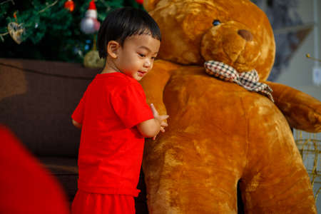 An Adorable toddler Asian baby boy (1-year-old) sitting on a chair and hugging a fluffy big bear doll with blurry celebration theme. Children's closeup portrait of activity and baby lifestyle conceptの写真素材