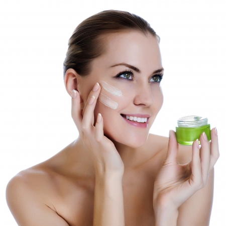 Happy smiling beautiful woman applying moisturizer cream on the faceの写真素材