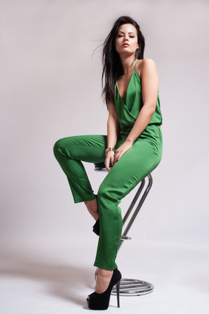 Fashion Dressed Sexy Girl Sitting on Chair. Full length Portrait. Beauty Woman isolated on White. Woman in Green playsuit and High Heelsの写真素材