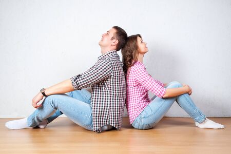 Young couple relaxing on the floor at home sitting barefoot back to back each looking up into the air with a thoughtful smile as they plan their future togetherの写真素材