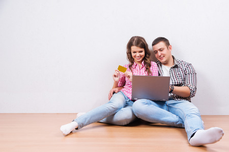 Shopping online together. Beautiful young loving couple shopping online while sitting on the floore togetherの写真素材