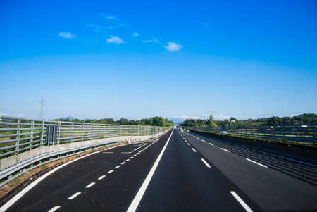 asphalt road through the green field and clouds on blue sky in summer dayの写真素材