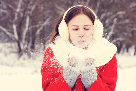 Beauty Winter Girl Blowing Snow in frosty winter Park. Outdoors. Flying Snowflakes. Sunny day. Backlit. Joyful Beauty young woman Having Fun in Winter Park. Defocusedの写真素材