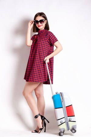 Full length of casual woman standing with travel suitcase - isolated on white backgroundの写真素材