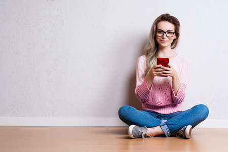 Happy beautiful woman sitting on the floor and using smartphoneの写真素材