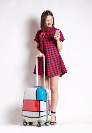 Full length of casual woman standing with travel suitcase - isolated on white backgroundの写真素材