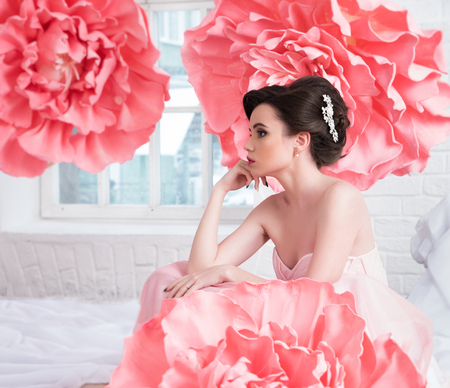 Beautiful sexy girl in a long dress with a huge pink flowers sitting by the window.の写真素材