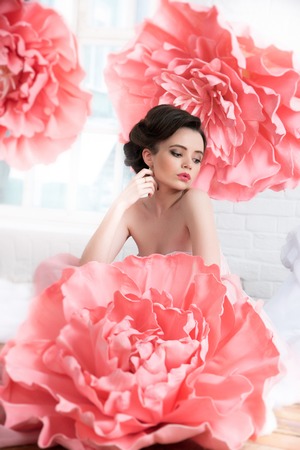 Beautiful sexy girl in a long dress with a huge pink flowers sitting by the window.の写真素材
