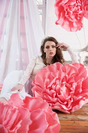 Beautiful sexy girl in a long dress with a huge pink flowers sitting by the window.の写真素材