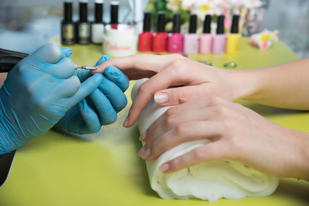 Closeup shot of a woman in a nail salon receiving a manicure by a beautician with nail file. Woman getting nail manicure. Beautician file nails to a customer.の写真素材
