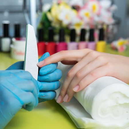 Closeup shot of a woman in a nail salon receiving a manicure by a beautician with nail file. Woman getting nail manicure. Beautician file nails to a customer.の写真素材