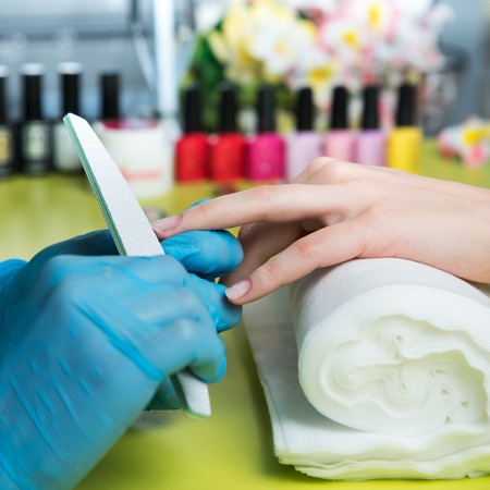 Closeup shot of a woman in a nail salon receiving a manicure by a beautician with nail file. Woman getting nail manicure. Beautician file nails to a customer.の写真素材