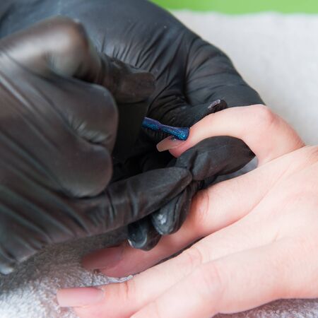 Closeup shot of a woman in a nail salon receiving a manicure by a beautician with nail file. Woman getting nail manicure. Beautician file nails to a customer.の写真素材