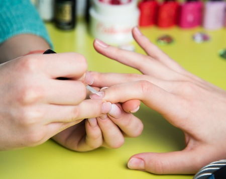 Closeup shot of a woman in a nail salon receiving a manicure by a beautician with nail file. Woman getting nail manicure. Beautician file nails to a customer.の写真素材