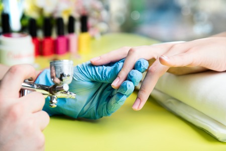 Closeup shot of a woman in a nail salon receiving a manicure by a beautician with nail file. Woman getting nail manicure. Beautician file nails to a customer.の写真素材
