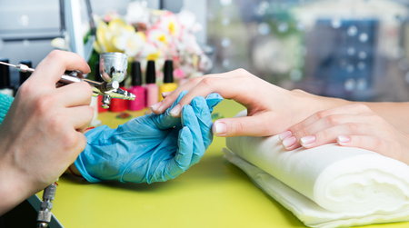 Closeup shot of a woman in a nail salon receiving a manicure by a beautician with nail file. Woman getting nail manicure. Beautician file nails to a customer.の写真素材