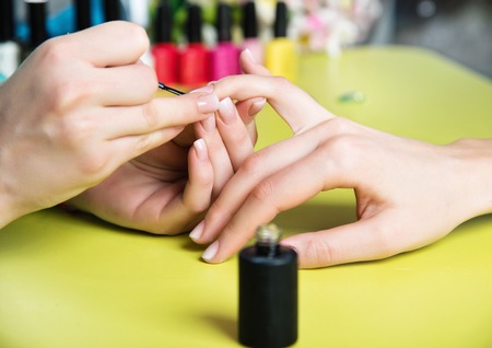 Closeup shot of a woman in a nail salon receiving a manicure by a beautician with nail file. Woman getting nail manicure. Beautician file nails to a customer.の写真素材