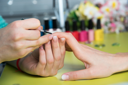 Closeup shot of a woman in a nail salon receiving a manicure by a beautician with nail file. Woman getting nail manicure. Beautician file nails to a customer.の写真素材