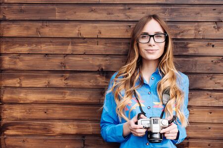 Happy young hipster woman in glasses holds retro photo cameraの写真素材