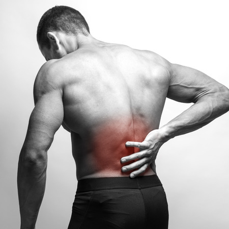 Male athlete with pain in his lower back, isolated in grey. Red spot around painful area.の写真素材