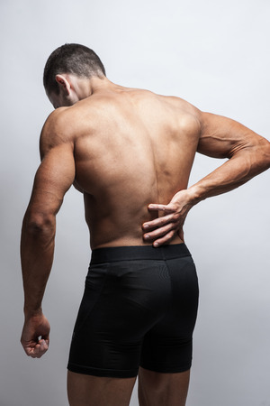 Male athlete with pain in his lower back, isolated in grey.の写真素材