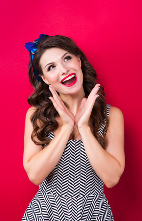 Beautiful young sexy pin-up girl with surprised expression, on red background.の写真素材