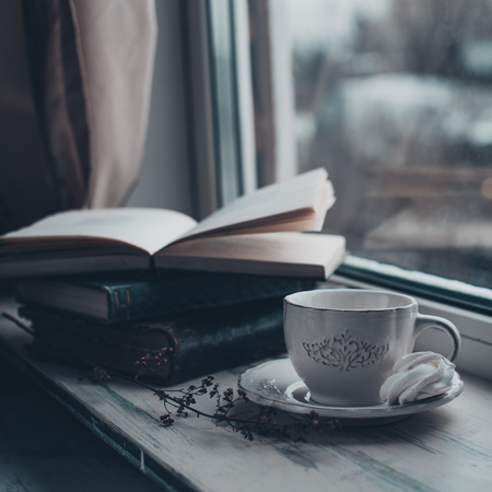 Cozy winter still life: cup of hot coffee and opened book on vintage windowsill against snow landscape from outside.の写真素材