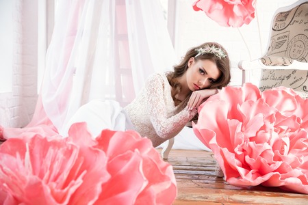 Beautiful sexy girl in a long dress with a huge pink flowers sitting by the window.の写真素材