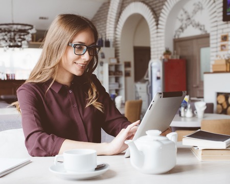 Concentrated at work. Confident young woman in smart casual wear working on laptop while sitting near window in creative office or cafe.の写真素材