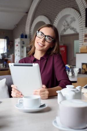 Concentrated at work. Confident young woman in smart casual wear working on laptop while sitting near window in creative office or cafe.の写真素材