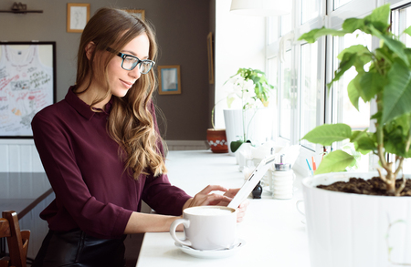 Concentrated at work. Confident young woman in smart casual wear working on laptop while sitting near window in creative office or cafe.の写真素材