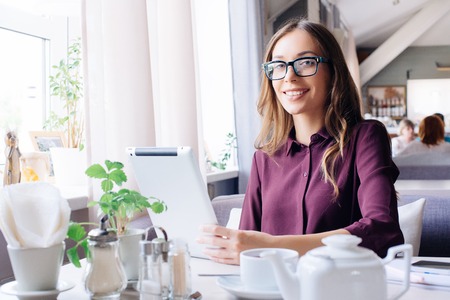 Concentrated at work. Confident young woman in smart casual wear working on laptop while sitting near window in creative office or cafe.の写真素材
