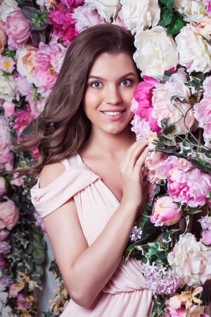 Beautiful romantic young woman in a wreath of flowers posing on a background of roses. Inspiration of spring and summer. Perfume, cosmetics conceptの写真素材