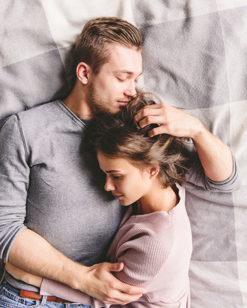 Pretty loving couple is luxuriating in bed together. They are hugging and smiling.の写真素材