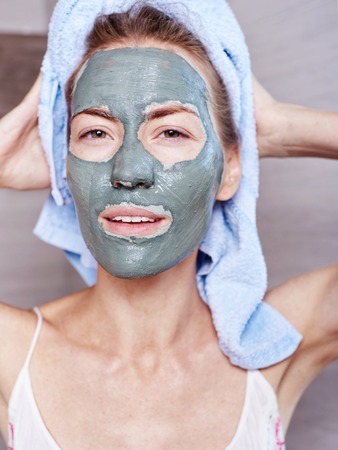 Woman applying mask moisturizing skin cream on face looking in bathroom mirror. Girl taking care of her complexion layering moisturizer. Skincare spa treatmentの写真素材