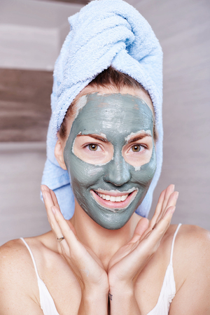 Woman applying mask moisturizing skin cream on face looking in bathroom mirror. Girl taking care of her complexion layering moisturizer. Skincare spa treatmentの写真素材