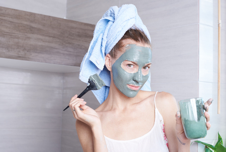 Woman applying mask moisturizing skin cream on face looking in bathroom mirror. Girl taking care of her complexion layering moisturizer. Skincare spa treatmentの写真素材