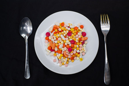 Colorful pills on white plate with spoon and fork on black backgroundの写真素材