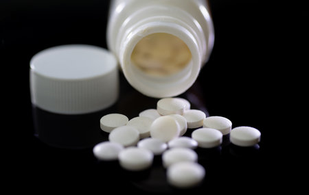 Pills spilling out of pill bottle on black background. Focus on foreground, soft bokeh.