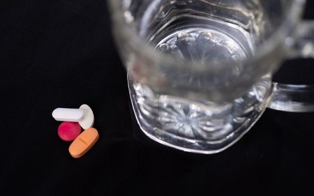 Pills and glass of water on black background. Focus on foreground.の写真素材