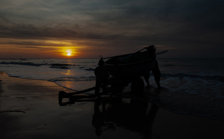 Silhouette of a fishing boat on the beach at sunset.の写真素材
