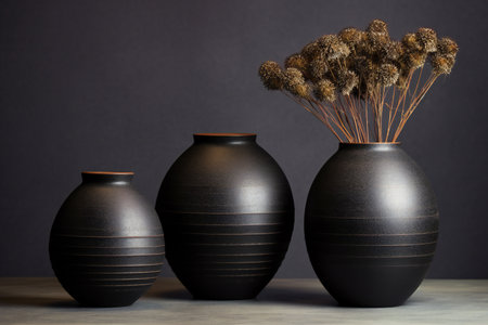 Three black vases with dried flowers on the table. Dark background.の素材